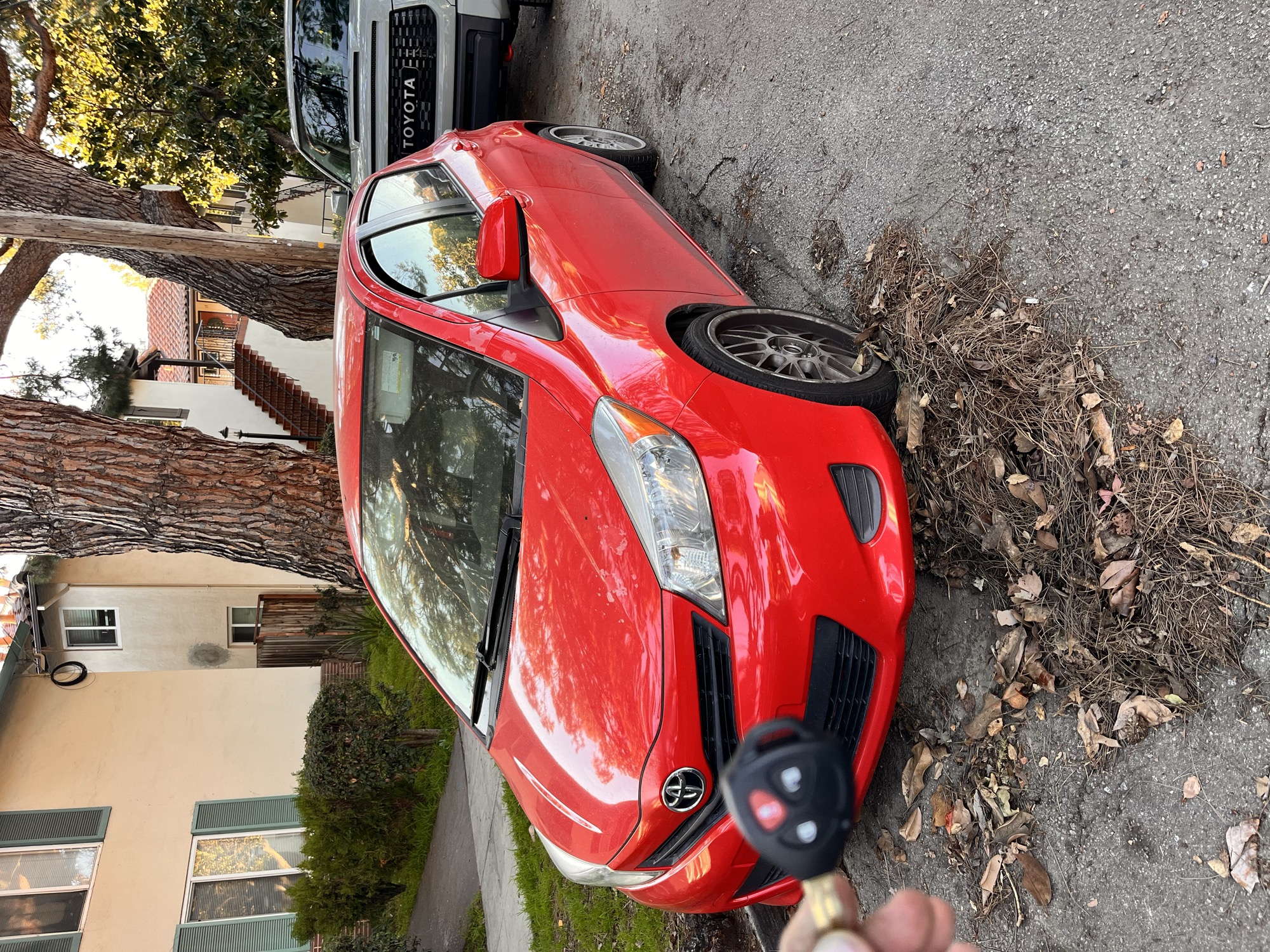 Car key fob held next to a red Toyota hatchback parked at the curb
