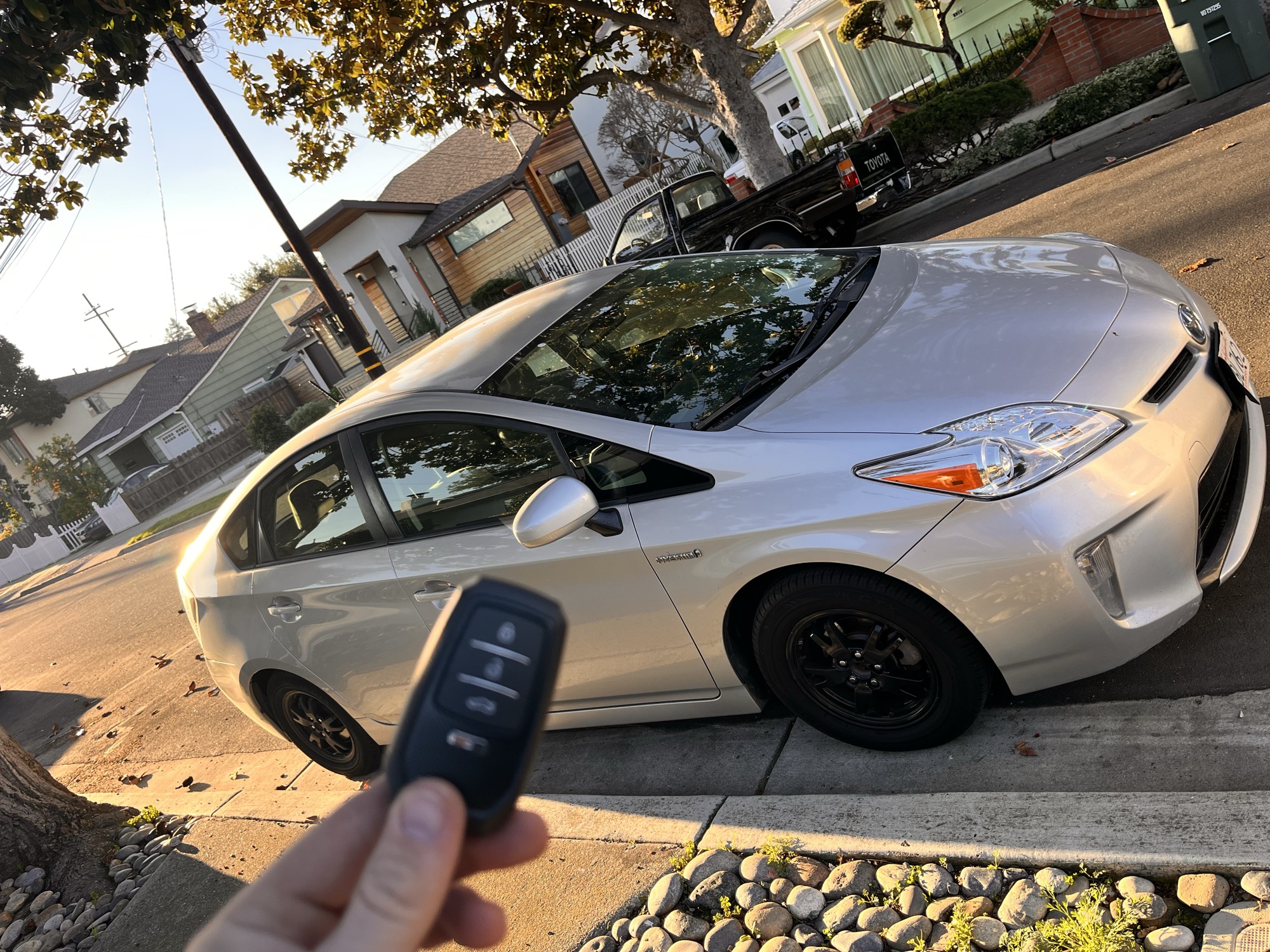 Replacement key fob for a silver Toyota Prius held next to the car
