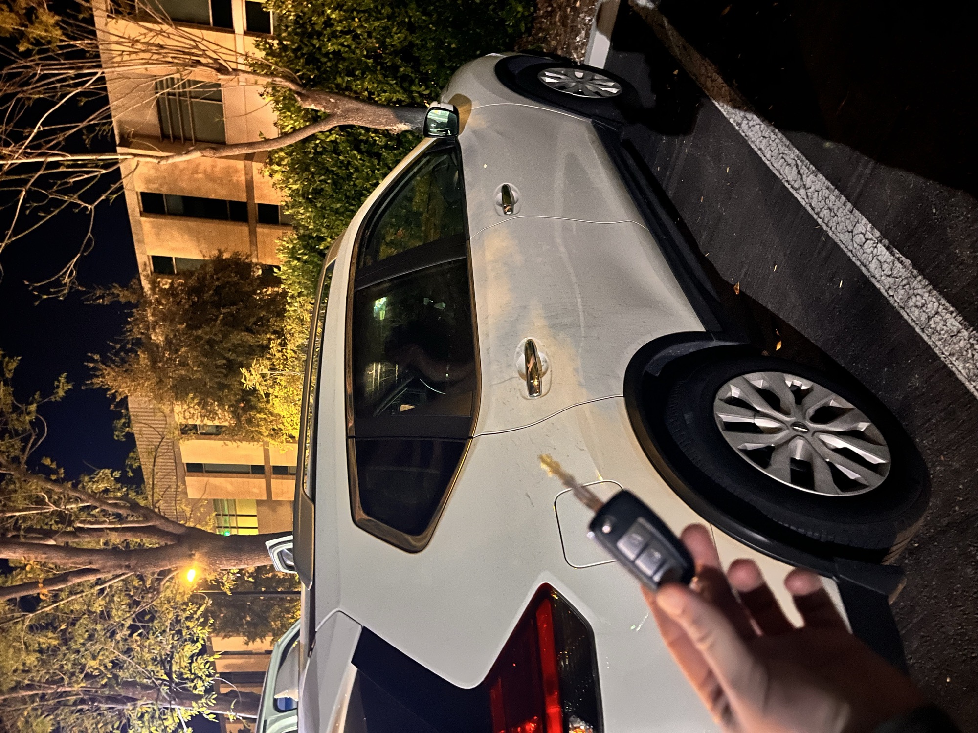 Car remote key held near the rear of a white SUV at night