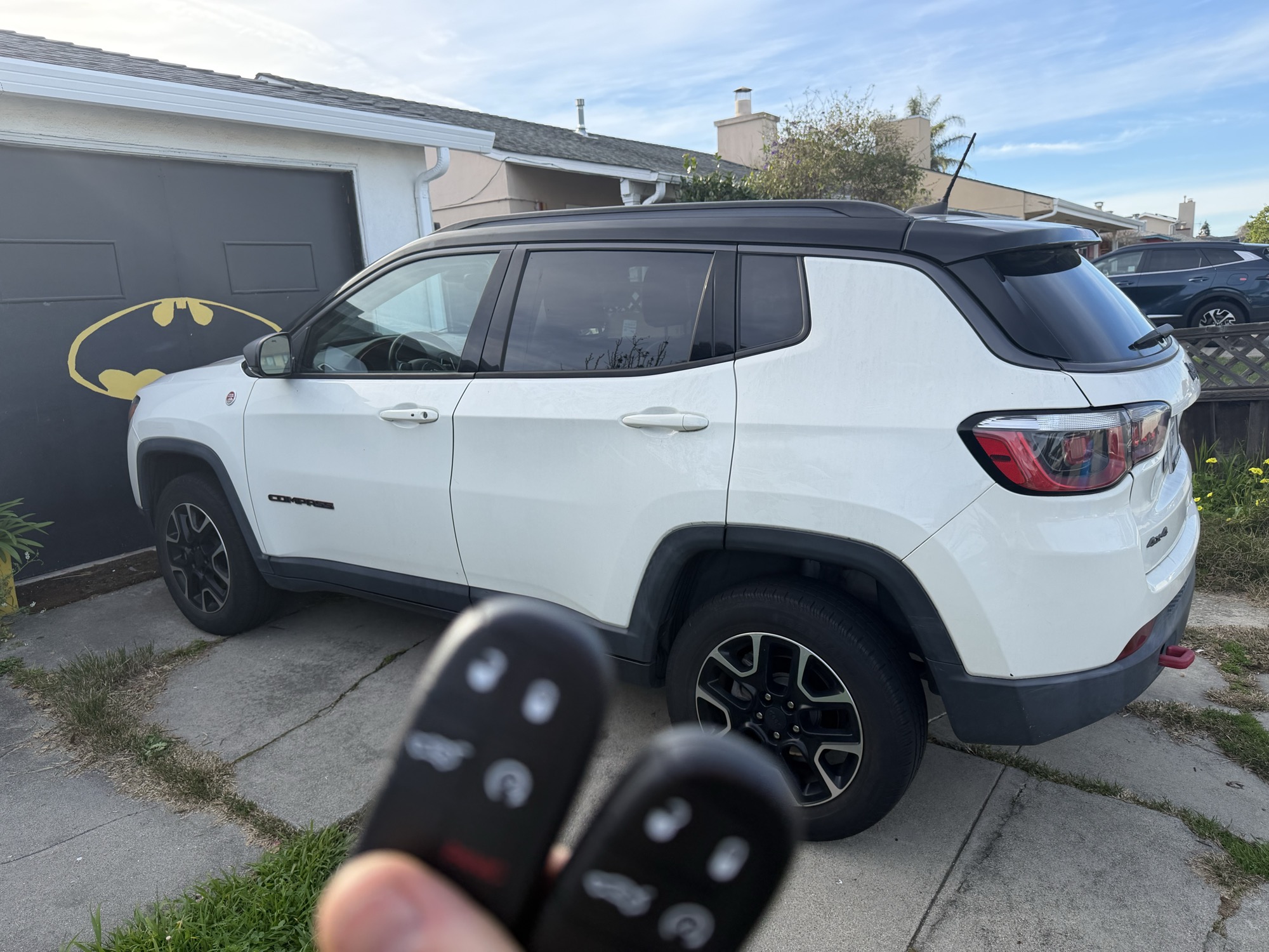 Two Jeep Compass key fobs held in front of a white Jeep SUV