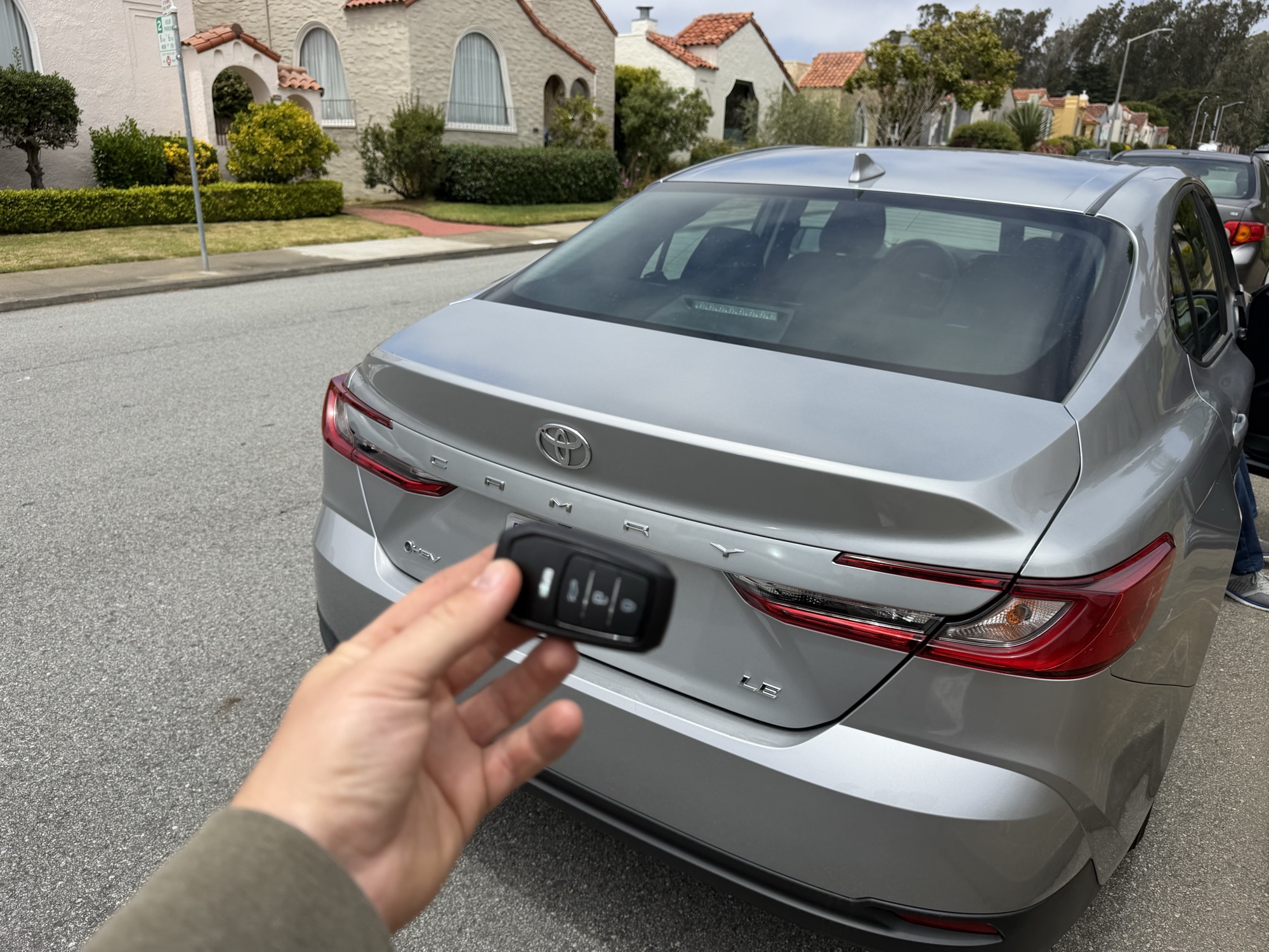 Replacement key fob held near a silver Toyota Camry hybrid